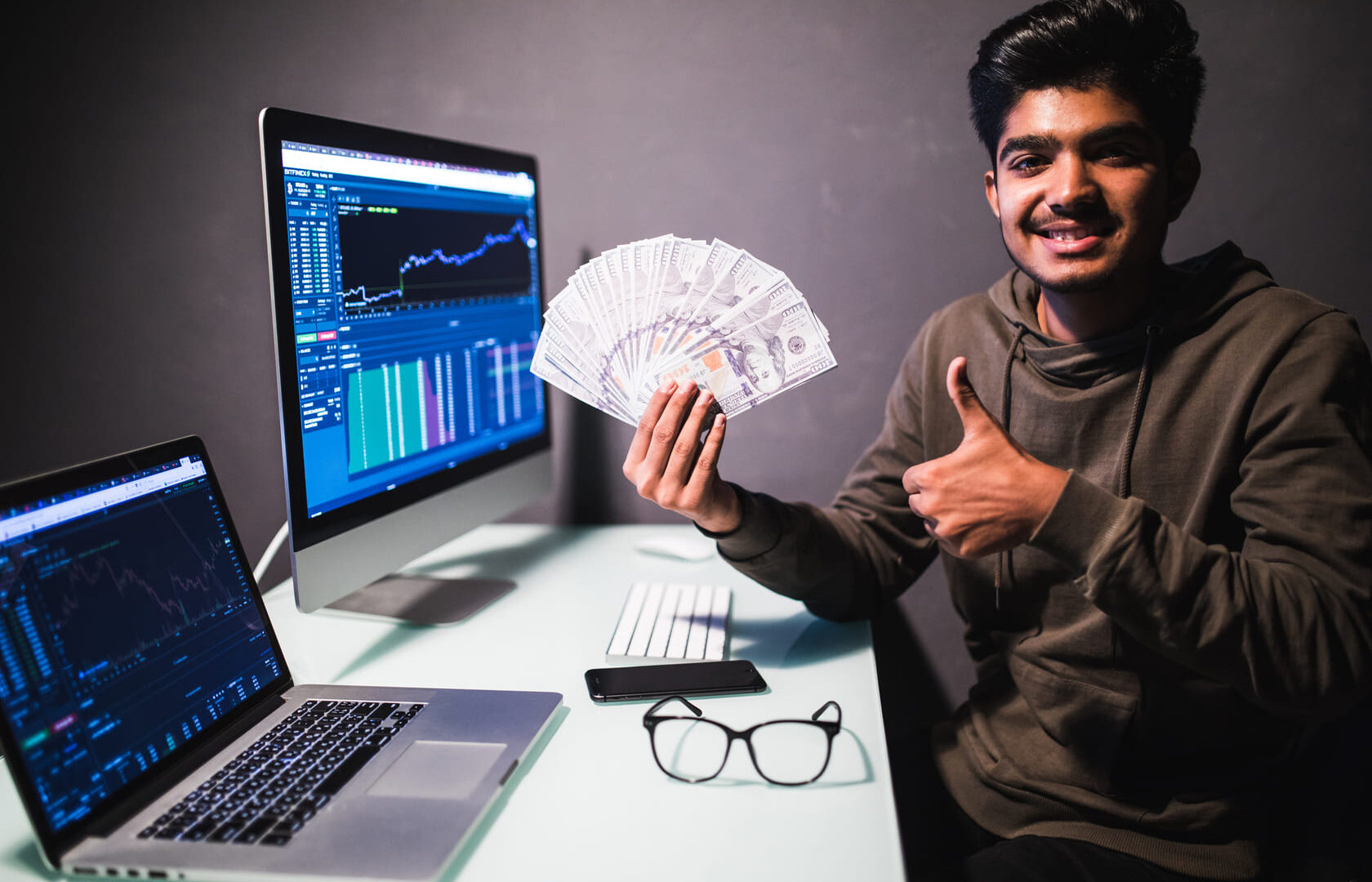 Young man showing how to make money with AI holding cash with a computer screen in the background