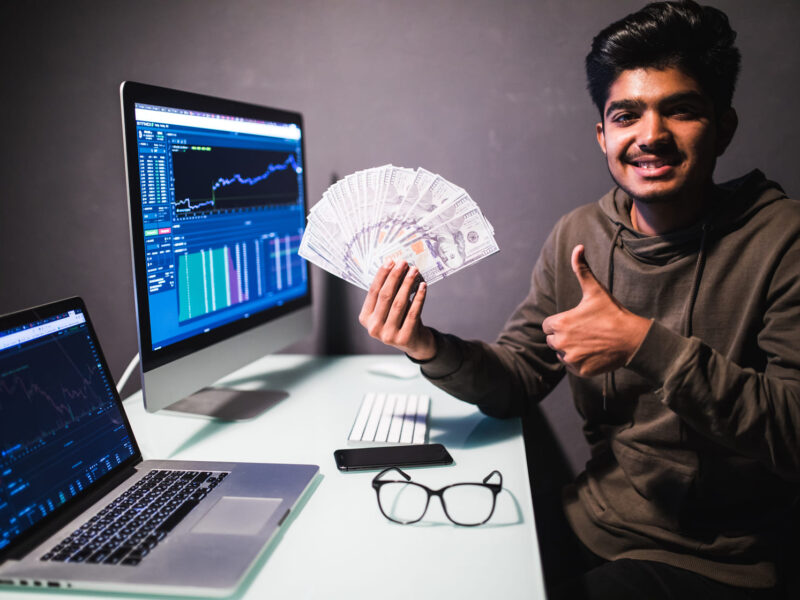 Young man showing how to make money with AI holding cash with a computer screen in the background